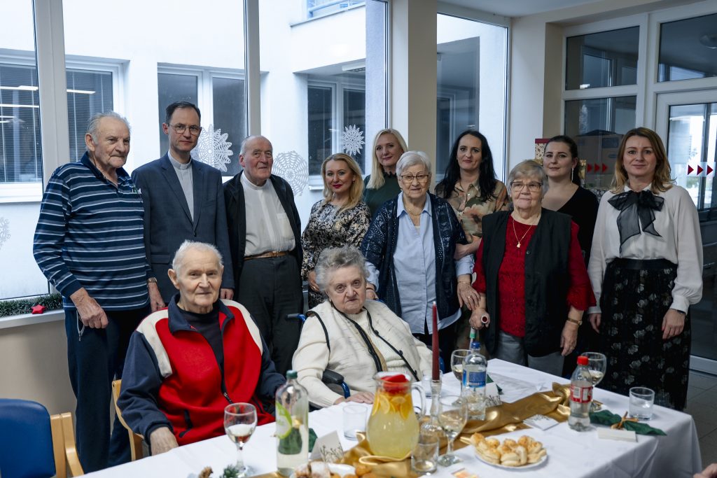 Spoločná fotografia seniorov, zamestnancov zariadenia a hostí počas vianočného posedenia v zariadení sociálnych služieb.